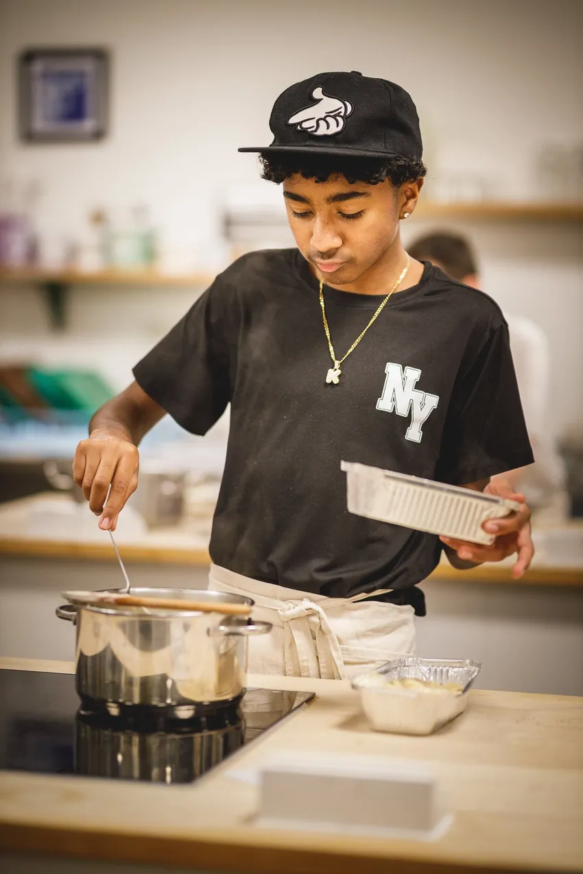 a boy in a black cap stirring a saucepan