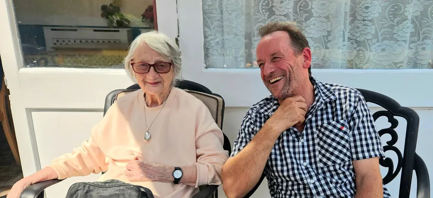 A care home resident and a befriender sit outside smiling together