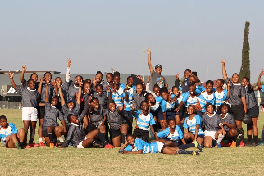 GWRI Group of young rugby players pose together on a rugby field after a match or training session, smiling, cheering, and making peace signs toward the camera