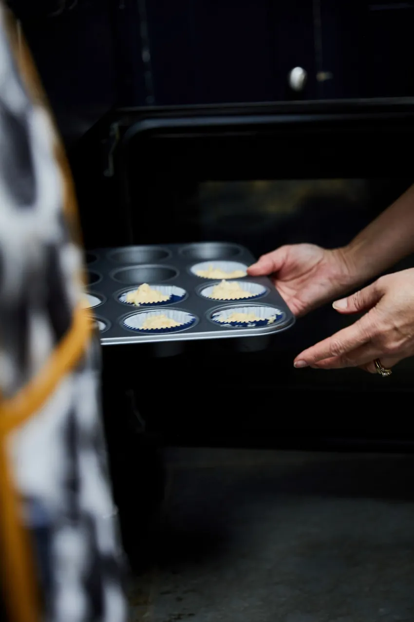 Woman putting cup cakes into an oven.