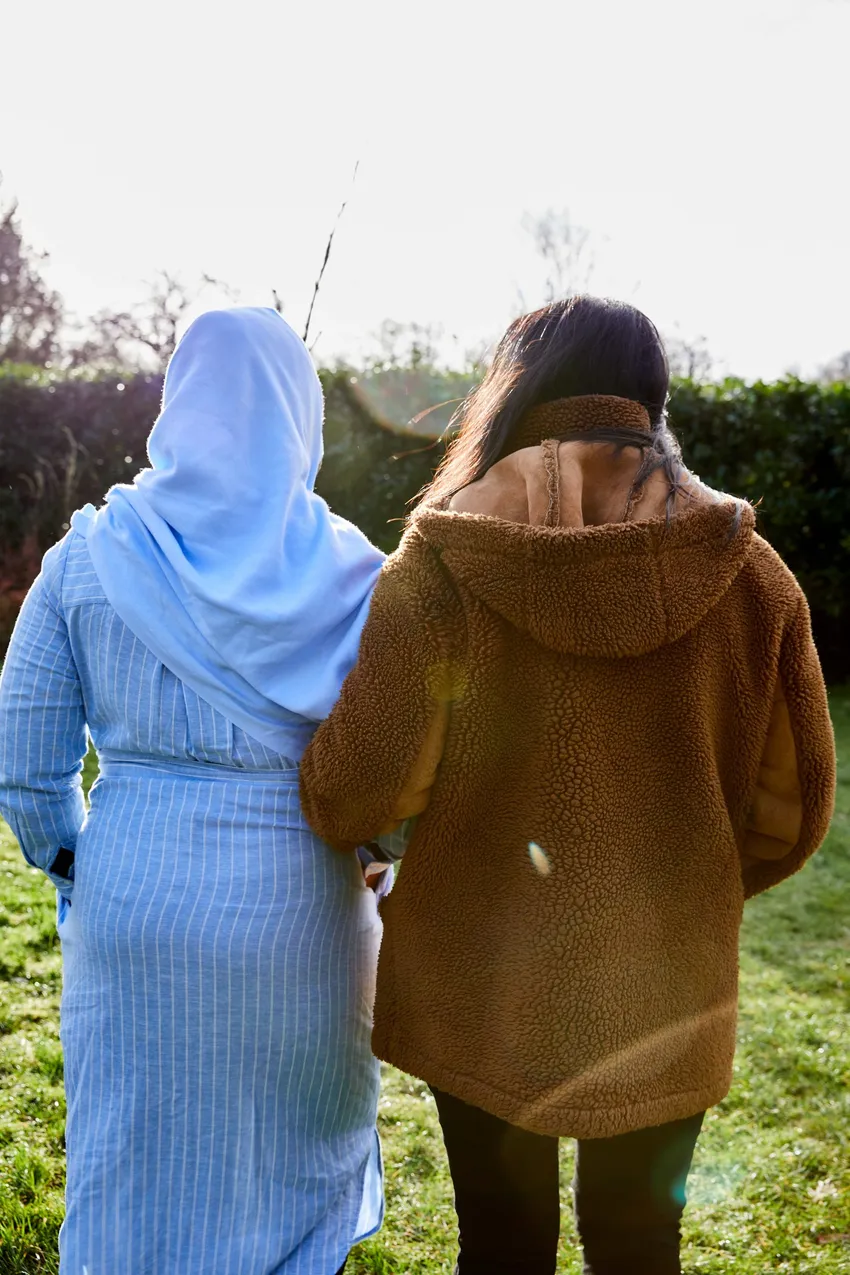 Two women walk arm in arm together outside.