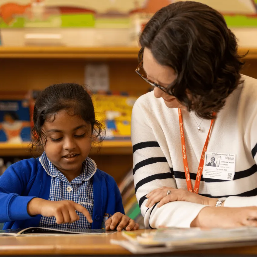 A Learn to Love to Read Volunteer reading with a primary school aged child. They are looking at the book together and the girl is pointing out words as she reads
