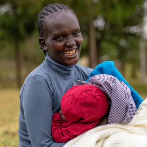 Woman holds her baby and smiles. Baby's face is hidden.