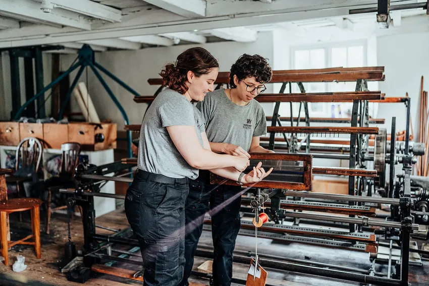 Two weavers operate the Mill’s warping drum, carefully threading fine silk through a reed.