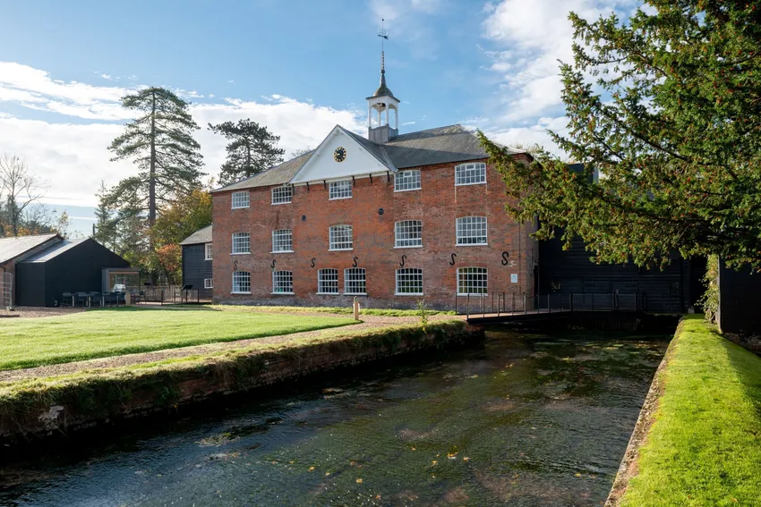 Photograph of the frontage of the Silk Mill. The River Test runs to the right. In front of the Mill is a lawn. The Mill is a three story building, with slate roof