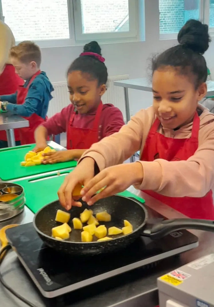 two young girls cutting and frying vegetables
