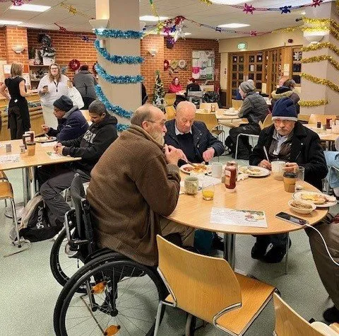 Image shows some of our guests during the period Christmas period. The is brightly lit and decorated with tinsel, through the doors you can see that it is dark outside.