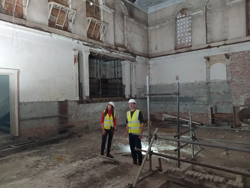 A man and a woman in hard hats and high vis, standing in the derelict Devizes Assize Court.